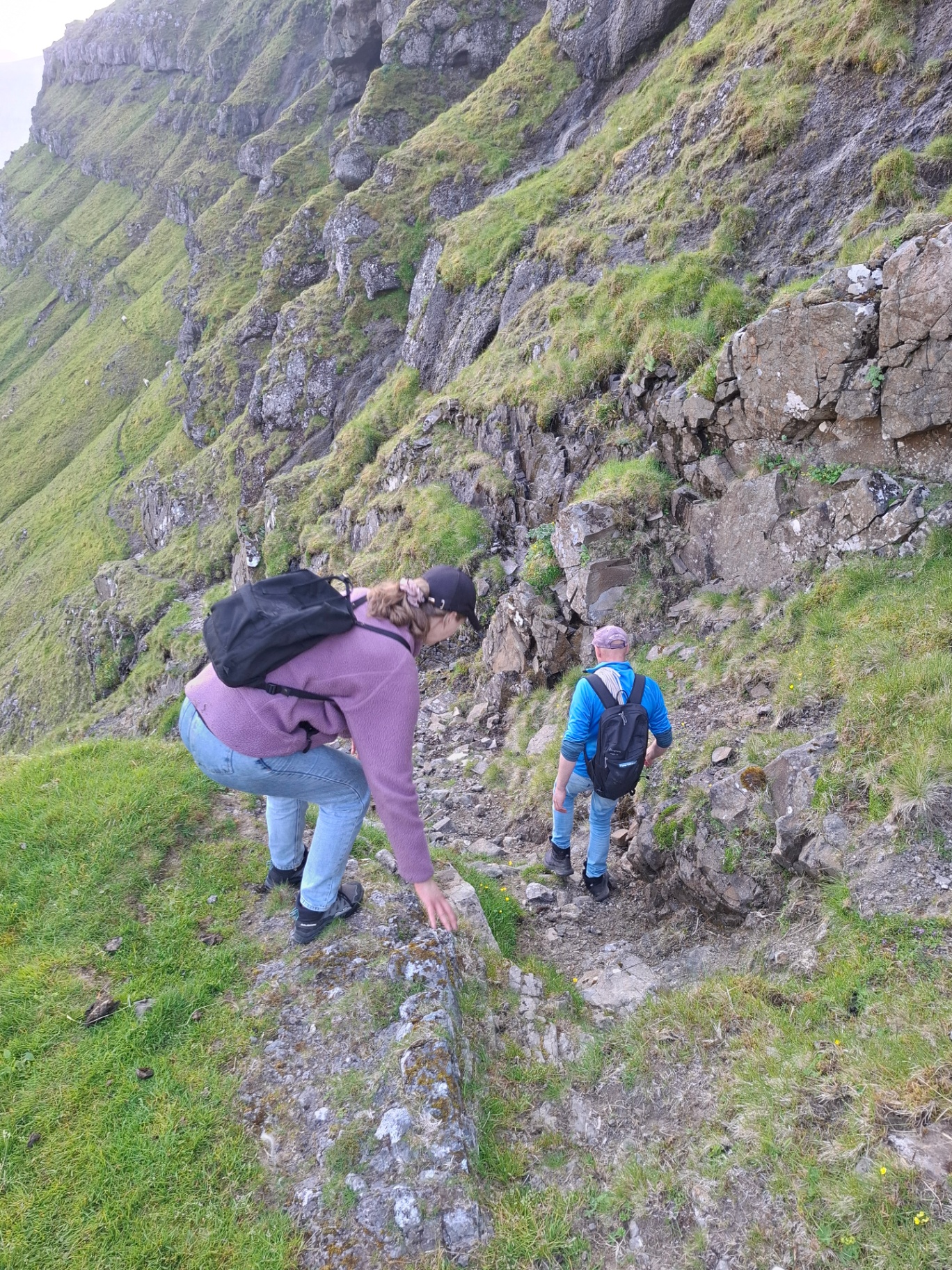Two hikers on a steep grass and basalt path in the Faroe Islands