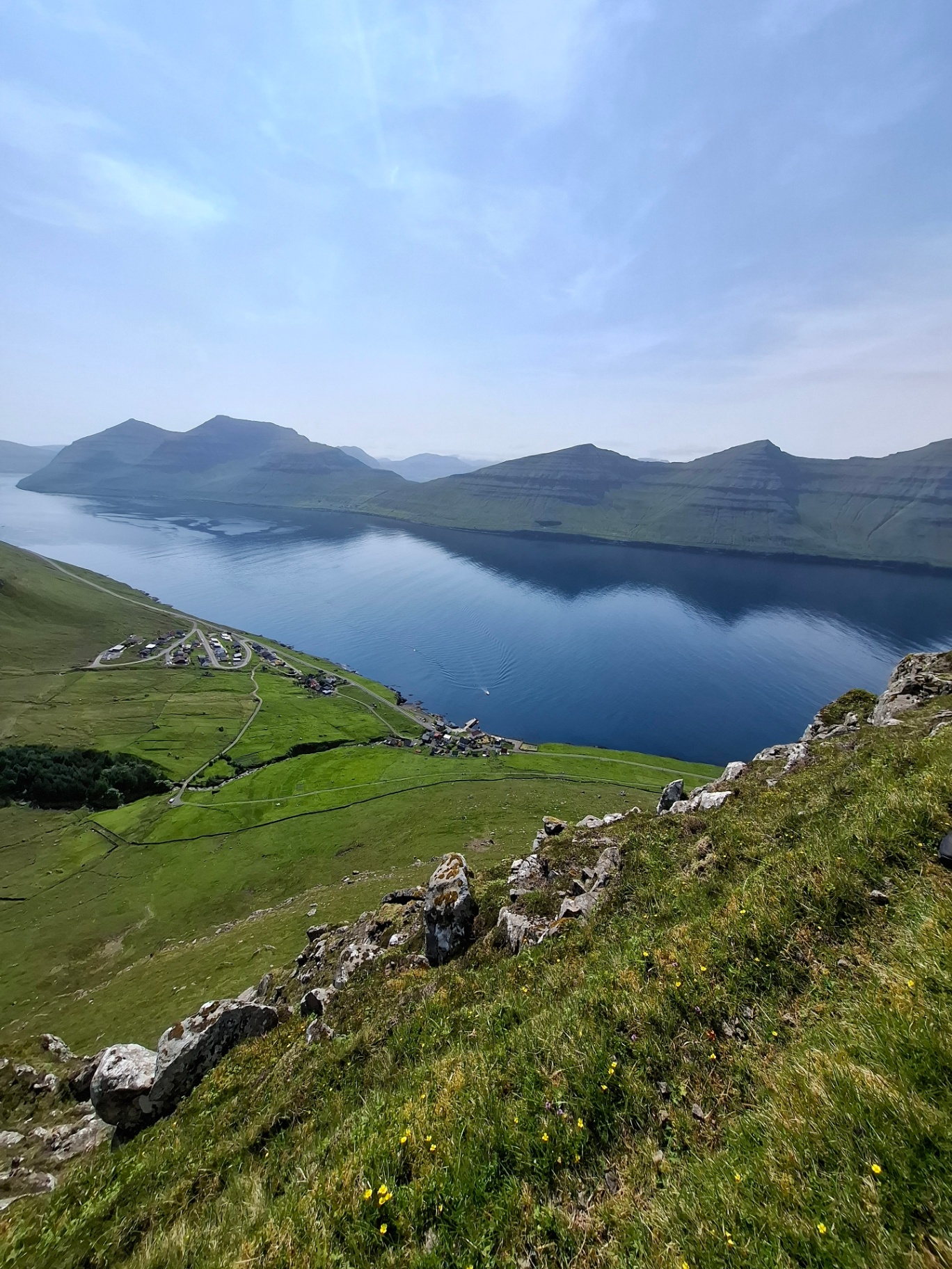Sunlit green ridge trail above turquoise Atlantic water in the Faroe Islands