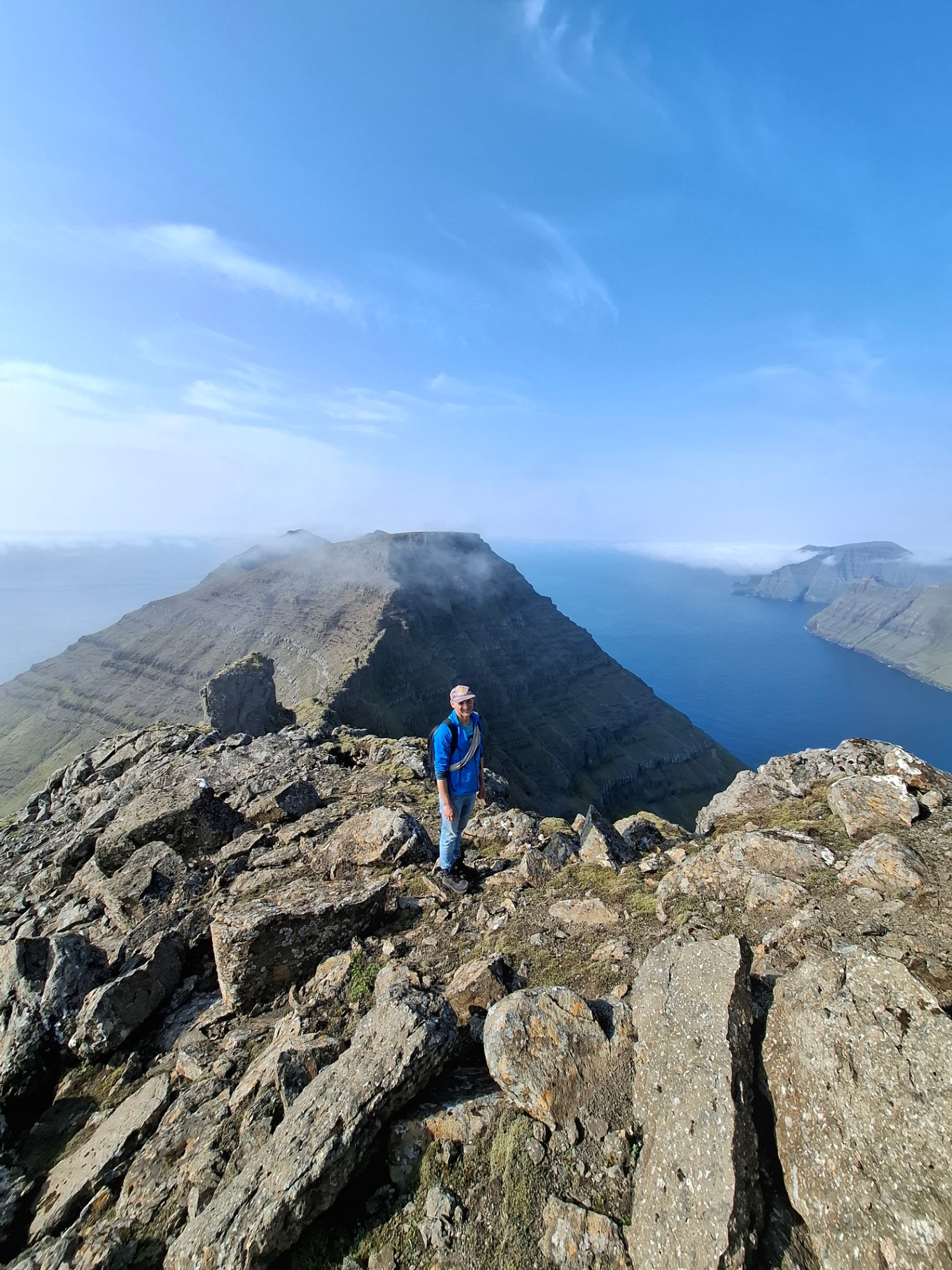 A hiker standing on a rocky summit ridge above the ocean